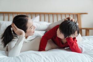Asian mom talking with son in bed