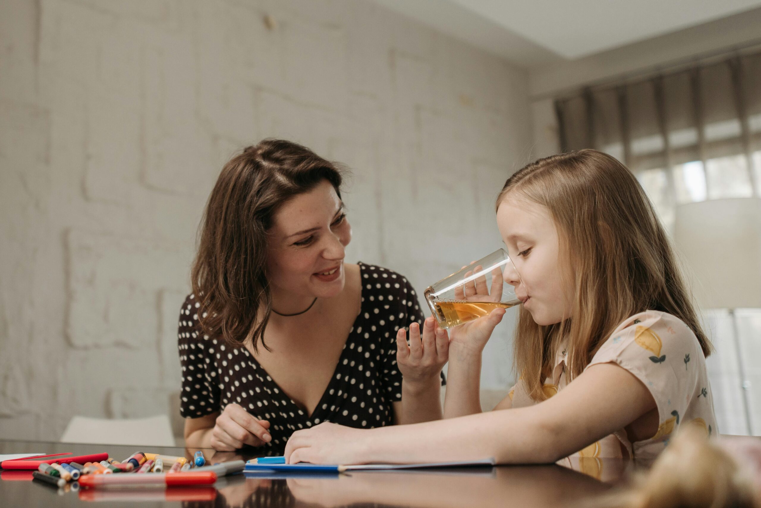 mom helping daughter drink at table