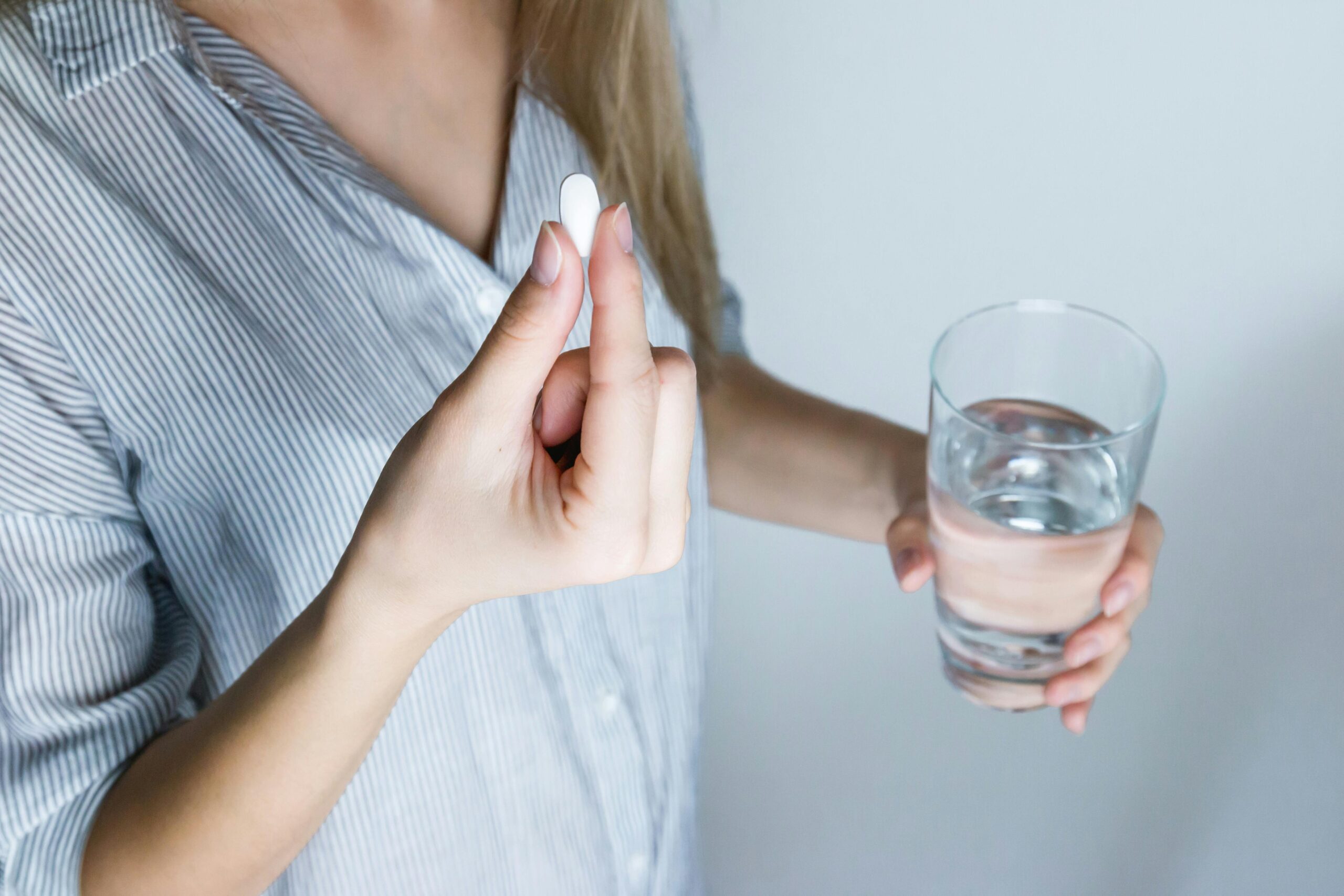 Woman's hand holding a pill and glass of water